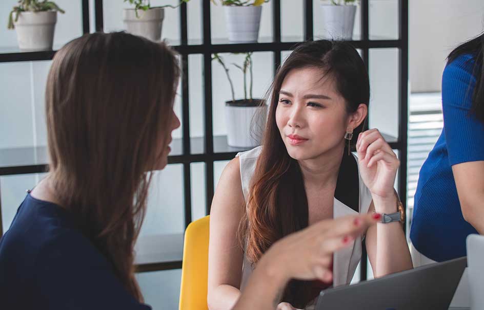 two women speaking in front of laptop